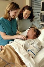 2 Nurses leaning over hospital bed with patient looking up.