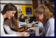 photo of two female high school students using a microscope
