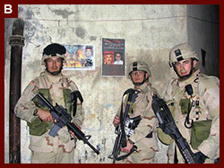 Capt. Michael Brian Daake and two members of his battalion, standing in front of 'Wanted' posters for Abu Musab Al-Zarqawi