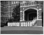 Graduates in white lined up out a building