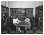 Two female students at a table in a library alcove
