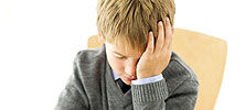 A boy sitting at a desk looking depressed and worried.