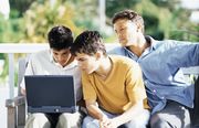 Three teenage boys looking at a laptop screen