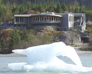 The curving window wall of Mendenhall Glacier Visitor Center overlooks the glacier and Lake Mendenhall, including an iceberg floating in the foreground.
