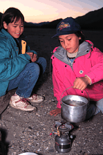 image of girls heating water pot on camp stove - Roger Kaye