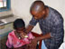 Photo of a clinical officer giving a 10-month-old his first dose of ACTs. (click here to see more)