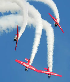 Four red stunt planes trailing smoke while flying.