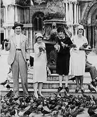 Vincent Price and 3 women standing before a fountain, each holding  a pigeon.