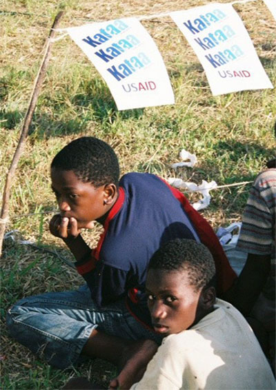 Photo of two children at the U.S. President's Malaria Initiative (PMI) kickoff for Tanzania with Kataa Malaria (Reject Malaria) posters in the background.