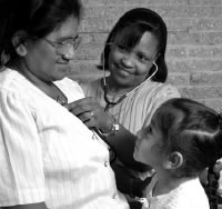 Health center physician listens to pregnant patient’s heart sounds and breathing with a stethoscope under watchful eye of patient’s smiling daughter