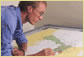 Photograph of man working on a large map on a light table.