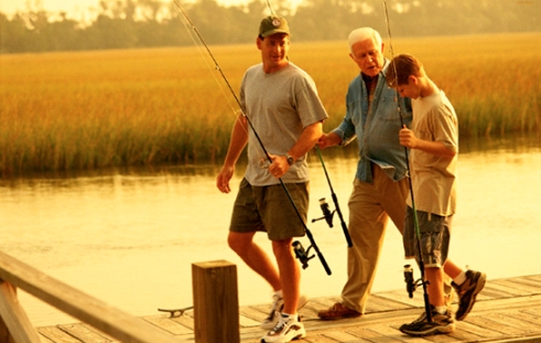 Photograph of grandfather, son and grandson walking on a dock with fishing poles.