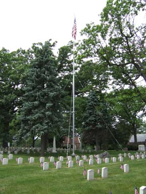 View of headstones at Forest Hill Soldiers’ Lot with flagpole at center; the graves are decorated with miniature flags for Memorial Day.