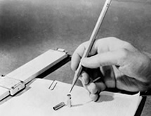 Photo of a hand holding a pencil over transistor and slide rule