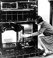 Photo of a woman kneeling at oven, with hand on the  open  oven door.