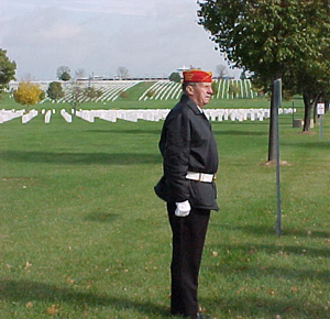 A photo of a member of the first all-volunteer Memorial Rifle Squad standing at attention on the cemetery lawn.  Upright markers are shown in the background.