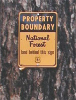 photo of a boundary sign posted to the bark of a tree.
