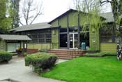 [photo]. Shows the front of the Weaverville Ranger Station. There is a green lawn and trees. There is an informational kiosk in the front of the building. Select for a larger photo.
