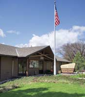 [photo]. Hayfork Ranger Station. The view shows the front of the building, a flag pole with the American flag, and a wooden sign. Select for larger photo.
