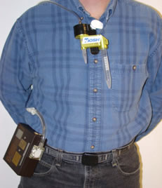 Worker standing wearing the sampler. One part is clipped to his collar, connected by a tube to a box attached to his belt.