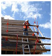 Worker high upon a 45 degree roof leaning on a NIOSH designed roof bracket safety rail system.