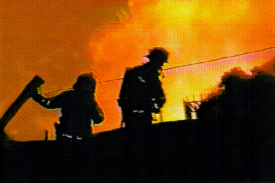 Two firefighters are shown silhouetted against the flame and smoke
at the fire scene