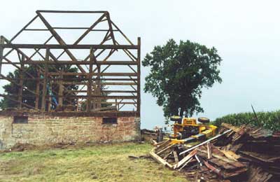 Photo 2 – View from the north side of the barn, showing the barn structure, the overturned forklift, and the broken rafter section lying next to the pile of discarded roofing.