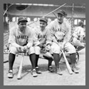 Three baseball players seated, with bats.