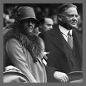 President and Mrs. Herbert Hoover standing in the stands in a stadium during a World Series baseball game, Mrs. Hoover looking toward the camera.