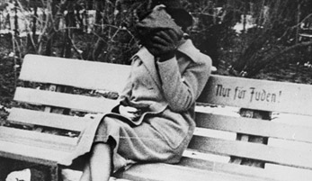A woman sits on a park bench marked "Only for Jews." Austria, ca. March 1938.