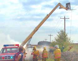 Photo 1 – View of firefighters at the scene, showing the forklift near the powerlines and the pump suspended by a wire rope cable.