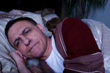 Photo of an angry man lying awake in bed.