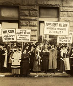 Women in a crowd, holding suffrage signs.