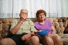 An overweight couple on the sofa eating popcorn.