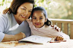 Image of older Hispanic woman with younf Hispanic girls, reading at a table.