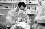 Photo of a dentist in a dental exam room with a 5-year-old child in the dental chair being treated and smiling