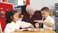 Photo of a female teacher watching two of her young students perform a task at school