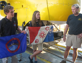 SCUBAnauts Collin Olson and Anna Moran display the Operation: Deep Climb banner and Explorer’s Club flag #61, with HURL Operations Director Terry Kerby looking on.