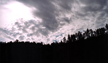 A photo of dark clouds gathering above a tree lined ridge.