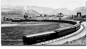 Historical photo with train pulling into Gardiner depot and Roosevelt Arch in the background.