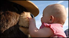 A small baby squeezing the nose of Smokey Bear.
