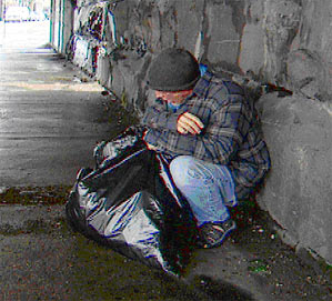 Image of a homeless man on the street with a garbage bag.
