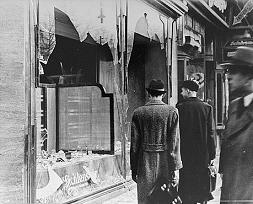 Germans pass by the broken shop window of a Jewish-owned business that was destroyed during Kristallnacht.