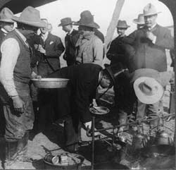 Phot: men in cowboy hats gathered around a cookfire.