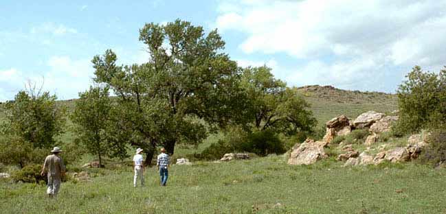 Three people cross open plains with trees on the Santa Fe Trail in the Oklahoma panhandle