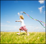 Foto: una niña corre por el campo haciendo volar una cinta