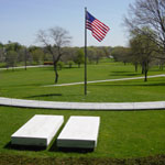 Two plain marble slabs and a U.S. flag on a green lawn.