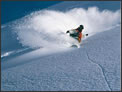 A picture of a snowboarder boarding through some deep powder, in an area that might have some avalanche potential. 
