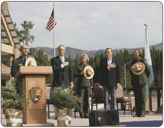 08-25-2006. Michael Breis sings the Star-Spangled Banner at Yellowstone 90th Anniversary Celebration and Launch of Centennial Challenge. Standing from left to right are Secretary Kempthorne, former NPS Director Mainella, Senator Thomas, and Yellowstone Superintendent Lewis. 
[NPS Photo by Bob Greenburg]