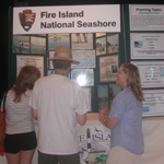 Three people observe and discuss exhibit panels.